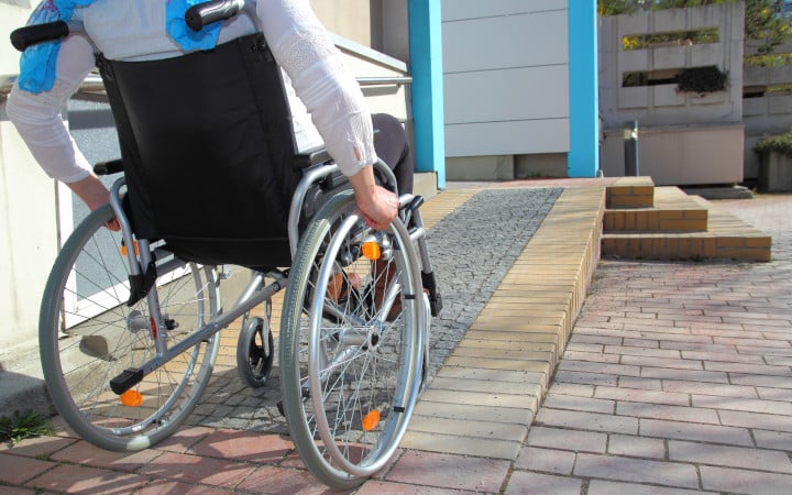 Personne à mobilité réduite utilisant une rampe adaptée pour les fauteuils roulants label Handibat