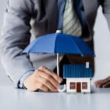 Assurance propriétaire non occupant représentée par un homme tenant un parapluie au dessus d'une maison