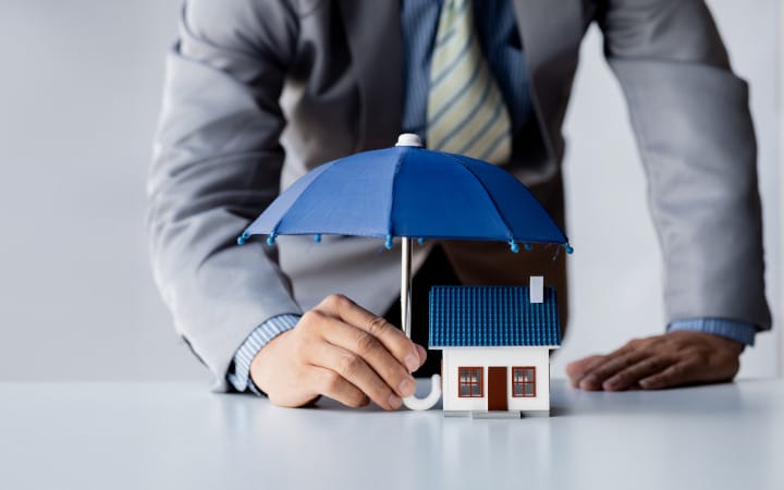 Assurance propriétaire non occupant représentée par un homme tenant un parapluie au dessus d'une maison